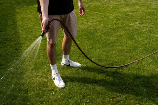 Person watering grass in a yard with a hose