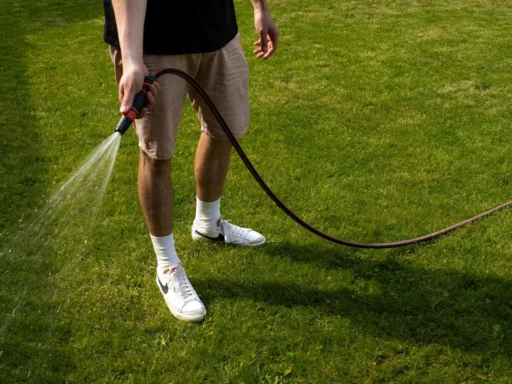 Person watering grass in a yard with a hose